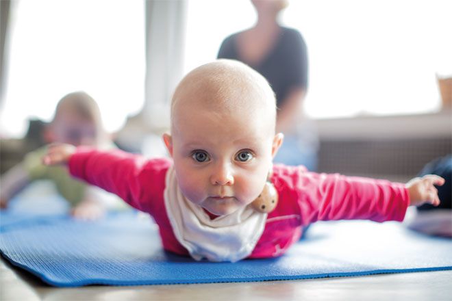 Foto: Ein Baby liegt auf dem Bauch und blickt in die Kamera. Es hat seine Arme weit zur Seite ausgestreckt.